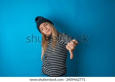 beautiful caucasian teen girl knitted  hat and striped T-shirt feeling angry, annoyed, disappointed or displeased, showing thumbs down with a serious look