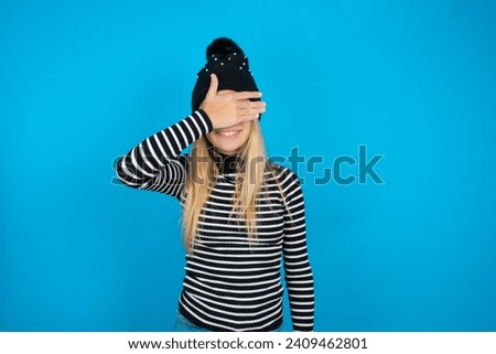 beautiful caucasian teen girl knitted  hat and striped T-shirt smiling and laughing with hand on face covering eyes for surprise. Blind concept.