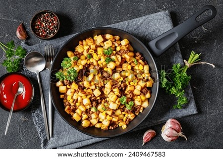 Beef Hash with roasted corn, garlic and parsley on a skillet on concrete table with ketchup, fork and spoon, horizontal view from above, flat lay Royalty-Free Stock Photo #2409467583