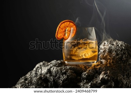 Smoked old fashioned rum cocktail with ice and dried orange slice on a grey stone. Royalty-Free Stock Photo #2409468799