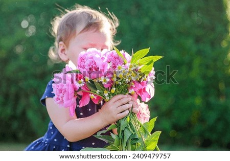 Little cute girl with a bouquet of peonies. A child holds a large bouquet of pink flowers. A girl smells flowers. Spring and summer. Children in nature.
