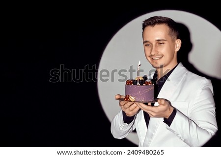 elegant caucasian man in white suit tuxedo holding cake with candle in the circle of light, copy space.