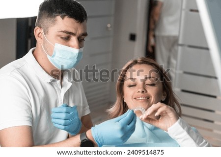Dentist holds aligner aligner in hands, preparing for important stage treatment and providing comfort to patient. Explains and demonstrates benefits aligner aligners for correcting alignment teeth Royalty-Free Stock Photo #2409514875