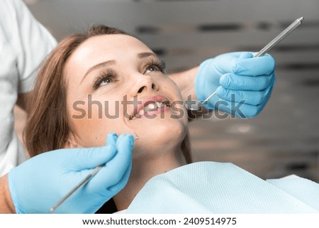 The patient expresses her satisfaction with a smile while sitting in comfortable dental chair. A dentist, choosing an individual approach, makes the procedure as comfortable and effective as possible. Royalty-Free Stock Photo #2409514975