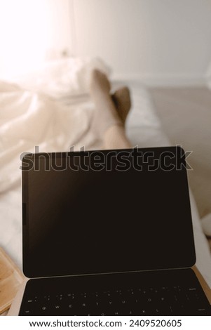 Image of laptop showing black screen display on lap, woman using tablet and working on white bed at home in day time.