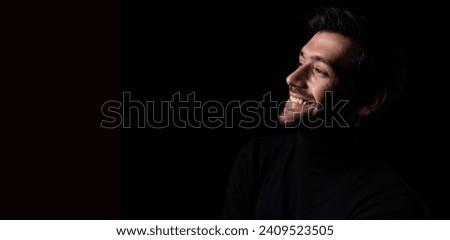 Happy Handsome man with a happy face standing and smiling with a confident smile showing teeth in the black background in the dark room Smiling man portrait Royalty-Free Stock Photo #2409523505