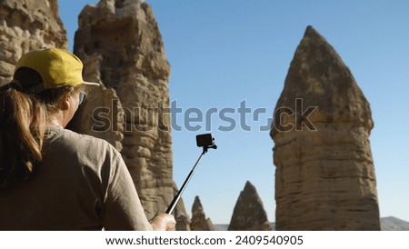 Woman filming herself on action camera against a backdrop of beautiful sandstone cliffs. A girl records a video for her blog from her holiday in Turkey. Love Valley in Cappadocia