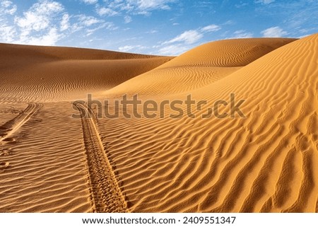 Landscape of Erg Admer in the Sahara desert, Algeria. A view of the dunes and ripples dug by the wind in the sand. The tracks of a 4x4 jeep sink into the dunes Royalty-Free Stock Photo #2409551347
