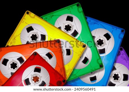 Colored transparent plastic compact audio cassettes lined up in a fan shape on a black background. Bright colors of the LGBT rainbow. The picture is suitable as a background for the music theme.