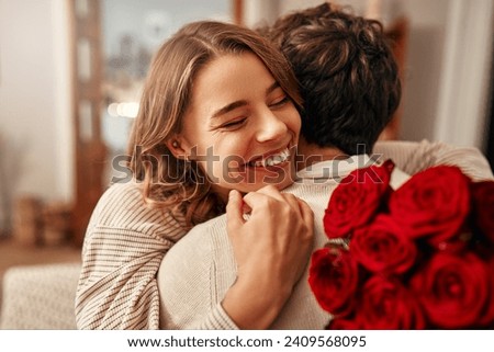 Happy Valentine's Day. A man gives a bouquet of red roses to his beloved woman in the living room at home, the woman hugging him tenderly. Romantic evening together. Royalty-Free Stock Photo #2409568095