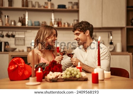 Happy Valentine's Day. A young couple in love with glasses of wine by candlelight sitting in the kitchen at the table, romantically spending the evening together. Royalty-Free Stock Photo #2409568193