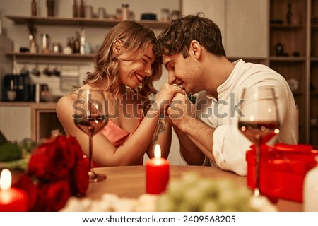 Happy Valentine's Day. A young couple in love with glasses of wine by candlelight sitting in the kitchen at the table, romantically spending the evening together. Royalty-Free Stock Photo #2409568205
