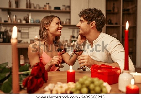Happy Valentine's Day. A young couple in love with glasses of wine by candlelight sitting in the kitchen at the table, romantically spending the evening together. Royalty-Free Stock Photo #2409568215