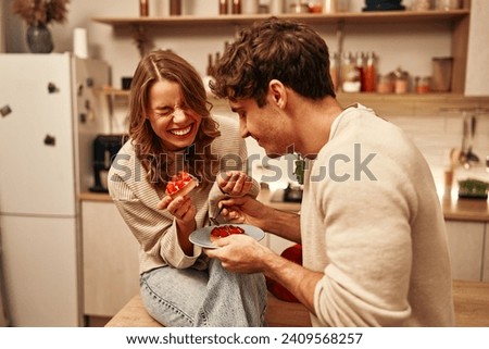 Happy Valentine's Day. Young couple in love eating cakes while sitting on the table in the kitchen, romantically spending the evening together. Royalty-Free Stock Photo #2409568257