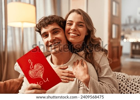 Happy Valentine's Day. A woman gives a greeting card to her beloved man with the inscription I love you in the living room at home. Royalty-Free Stock Photo #2409568475