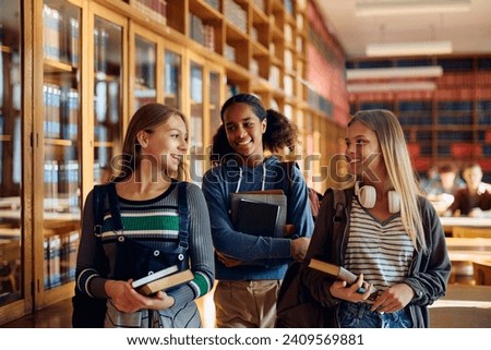 Group of happy teenage girls communicating at high school library. 