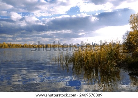 Beautiful autumn landscape in the Obolonsky district of Kyiv. Yellowed trees on the banks of the Dnieper River against a background of blue clouds.