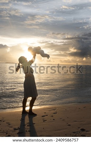 Beautiful woman throw up her baby on the beach on sunset. Silhouettes