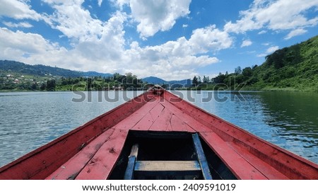 The tip of a red boat in Lake Kivu Rwanda Congo contrasts with green mountains and villages in the background against clear blue sky in summer.