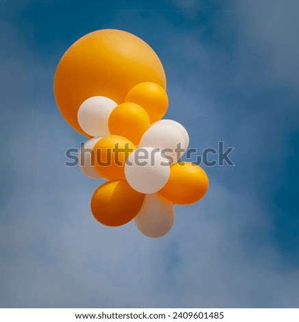 Large and small orange and white balloons against a blue sky with clouds 
