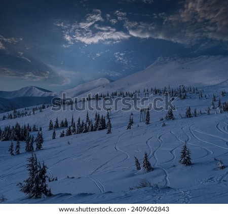 Alpine resort ski lift with seats going over the pre sunrise night mountain skiing freeride slopes and fir tree groves. Svydovets ridge view from Dragobrat ski resort.