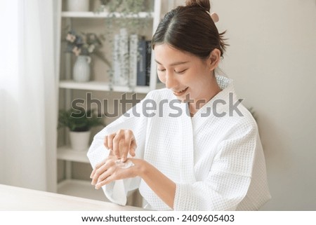 Health care, beauty smile pretty asian young woman in bathrobe, towel after shower bath at home, finger applying moisturizer on her back hand. Skin body cream moisturizing lotion, routine in morning.