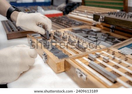 The worker selects gauge blocks to obtain the required control size of the part being manufactured and adjusts the measuring tool of a CNC metal-cutting machine. Royalty-Free Stock Photo #2409613189