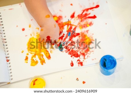 Child toddler dips his finger into cans of paint and draws in an album on paper, finger paints, children's development