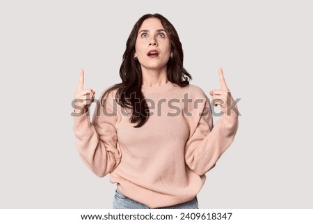 Young Caucasian woman in a studio setting pointing upside with opened mouth.