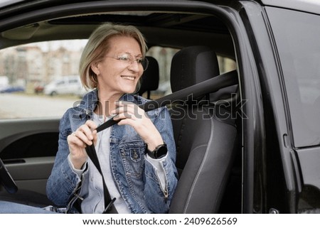 mature blonde woman sits in car and fastens seat belt