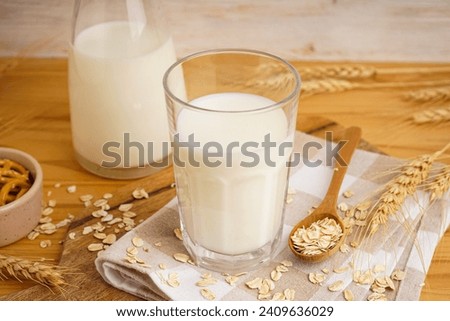 Glass and jug of fresh milk on wooden table against color background, with oatmeal. Royalty-Free Stock Photo #2409636029