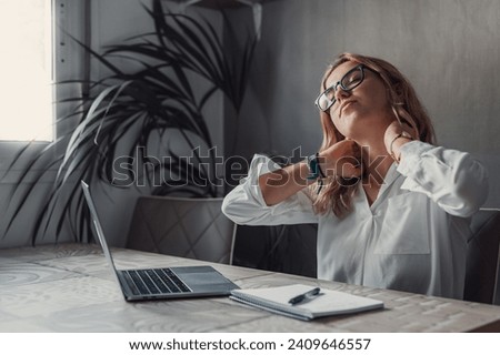 Exhausted young Caucasian female worker sit at desk massage neck suffer from strain spasm muscles. Tired unwell woman overwhelmed with computer work sedentary lifestyle struggle with back pain or ache Royalty-Free Stock Photo #2409646557