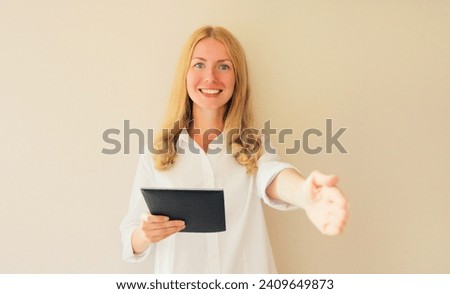 Happy smiling caucasian professional woman employer stretches out her hand for handshake greets applicant holds digital tablet computer or folder with paper documents in office