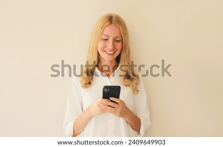 Portrait of happy smiling caucasian young woman 20s with mobile phone looking at device on studio background