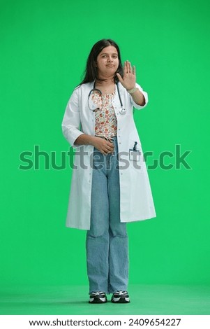 A female doctor on a green background, in full height, shows a stop sign