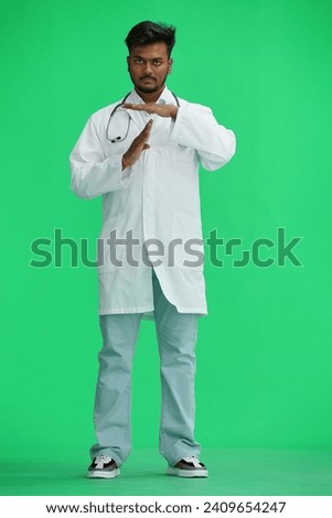 A male doctor, on a green background, in full height, shows a pause sign