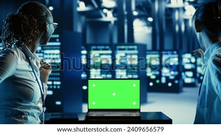 IT developers running code on green screen laptop, troubleshooting data center equipment. Technicians using chroma key device to monitor server cabinets, networking systems and storage arrays Royalty-Free Stock Photo #2409656579