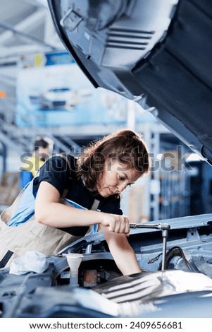 Technician in car service uses torque wrench to tighten bolts after replacing engine. Diligent auto repair shop employee uses professional tools to fix customer automobile Royalty-Free Stock Photo #2409656681