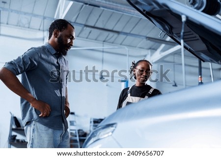 Mechanic at auto repair shop conducts annual vehicle checkup, informing customer about needed steering mechanism replacement. Competent garage worker talks with customer after finishing car inspection Royalty-Free Stock Photo #2409656707