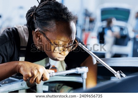 African american engineer does client car maintenance in auto repair shop using lamp light after vehicle shut down unexpectedly. Trained expert in garage mending customer damaged automobile fuel tank Royalty-Free Stock Photo #2409656735