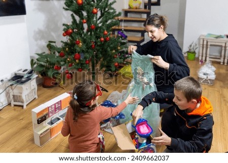 Merry Christmas and Happy New Year! Beautiful mom and her children  are smiling while opening Christmas presents. Christmas gift, presents for New Year. 