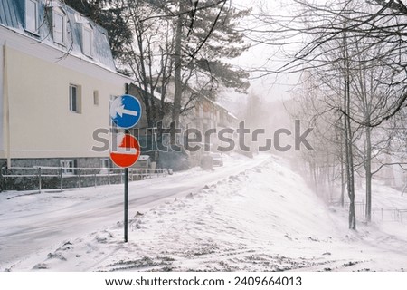 Stop and detour road signs stand on a snowy street near a building