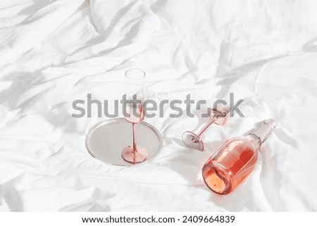 Pink champagne glasses with metal shiny and bottle of rose sparkling wine on white bed cloth. Lifestyle aesthetic photo, star filter effect. Valentine's Day holiday, love concept, romance meeting.