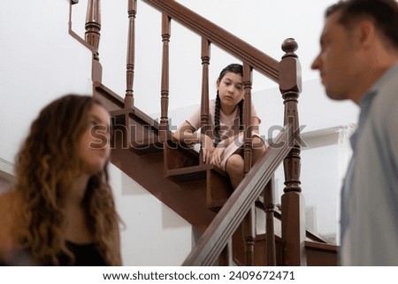 Stressed and unhappy young girl watch her parent arguing from the stair. Domestic violence at home and traumatic childhood develop to depression and anxiety. Unhealthy family concept. Synchronos Royalty-Free Stock Photo #2409672471