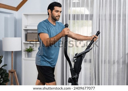 Athletic and sporty man running on elliptical running machine during home body workout exercise session for fit physique and healthy sport lifestyle at home. Gaiety home exercise workout training. Royalty-Free Stock Photo #2409677077