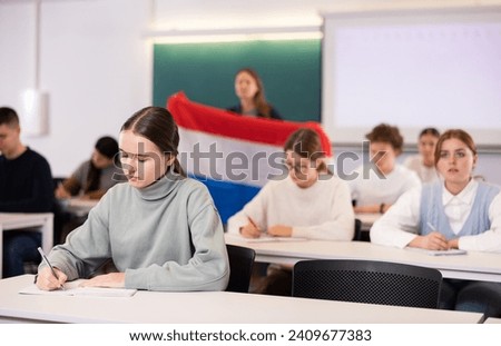 A young female student is carefully recording a lecture by a school teacher Royalty-Free Stock Photo #2409677383
