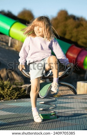 A cute blonde girl is sitting on a swing in the playground. The concept of a happy childhood.