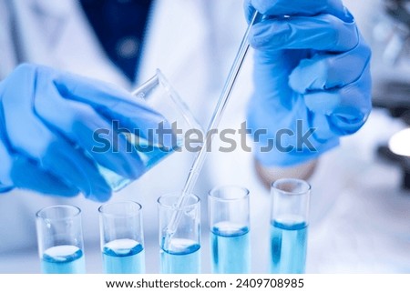 Woman research scientist biology chemistry medicine pouring liquid from beaker to test tube indoor science laboratory room, adult female person blue glove work discovery experiment medical chemist