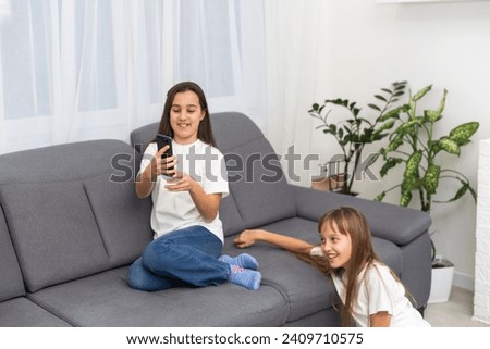 Two cute Caucasian blonde girls sisters holding cell phone and laughing.