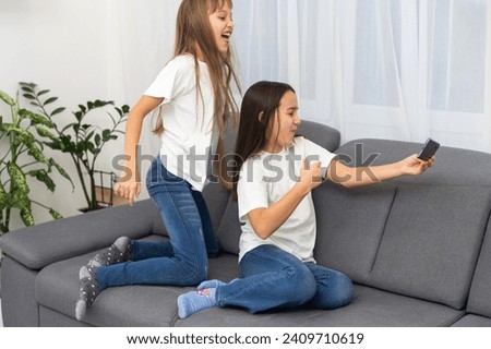 Happy schoolgirl lying near her friend and using new smartphone for chat